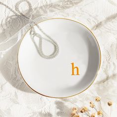 a white and gold plate with the letter h on it, next to dried flowers