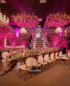 a long table with white chairs and pink flowers on it