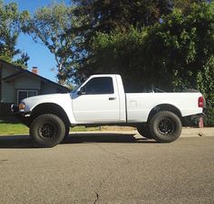 a white pick up truck parked on the side of a road in front of a house