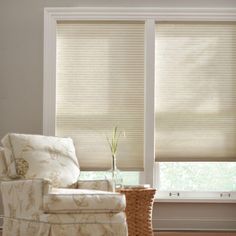 a living room with two windows and a chair in front of the window that has blinds on it