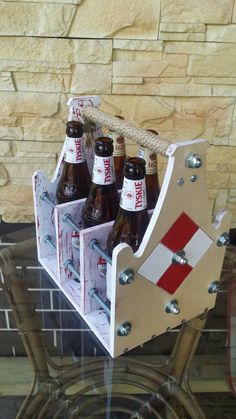 six beer bottles in a wooden holder on a glass table next to a brick wall