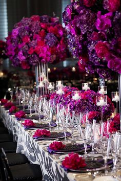 a long table with purple and red flowers on it is set up for a formal function