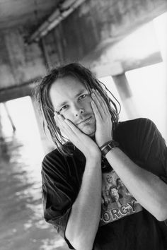 a man with dreadlocks standing in front of a body of water holding his hands to his face