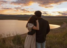 a man and woman standing next to each other in front of a lake