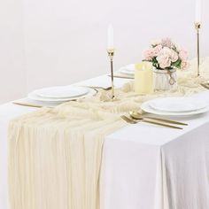 the table is set with white plates and silverware, candles and flowers in vases