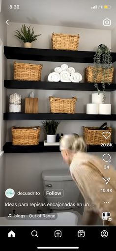 a woman standing in front of a toilet next to shelves filled with towels and plants