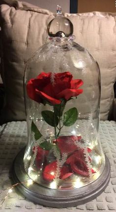 a red rose in a glass dome with fairy lights on the bottom is sitting on a table