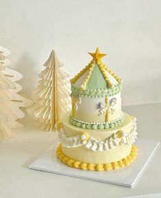 a three tiered cake sitting on top of a table next to a christmas tree