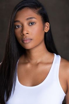 a woman with long black hair wearing a white tank top and looking at the camera