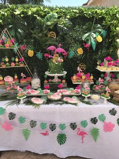 a table topped with cakes and desserts covered in green leafy plants next to a wall