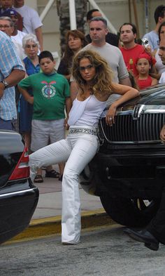 a woman sitting on the hood of a car in front of a group of people