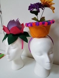 two white mannequin heads with colorful hats on their heads, one has flowers in it