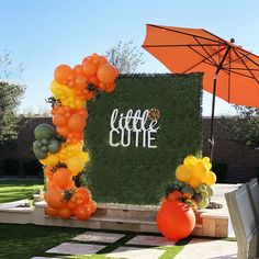 an orange and yellow balloon arch with the words little cutie on it in front of a green backdrop