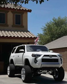 a white toyota truck parked in front of a house with an american flag on the roof