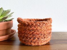 a small crocheted basket next to a succulent plant on a wooden table