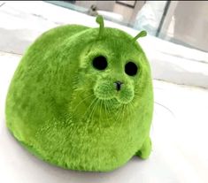 a green stuffed animal sitting on top of a white surface next to a window sill