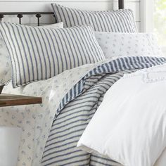 a bed with blue and white striped comforter next to a night stand in front of a window