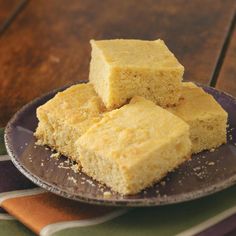 three pieces of cornbread on a plate next to a striped napkin and spoons