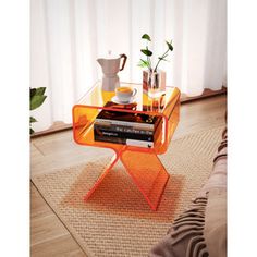 an orange glass side table with books and cups on it in front of a window