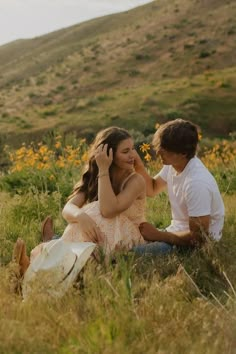 two people sitting in the grass talking on their cell phones