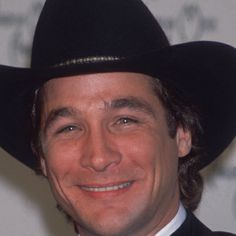 a man wearing a black cowboy hat smiles at the camera