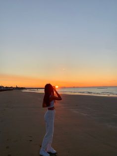 a woman standing on top of a sandy beach next to the ocean at sun set