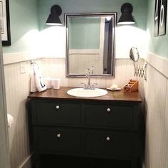 a bathroom with a sink, mirror and lights on the wall next to a toilet