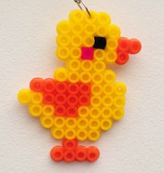 a yellow and red bird made out of legos on a white surface with a metal hook