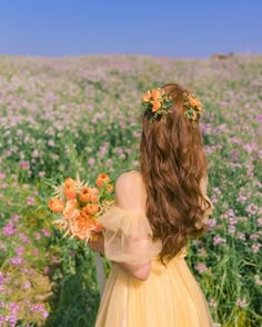 a woman in a yellow dress is standing in a field full of flowers with her back to the camera