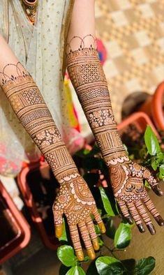 a woman's hands with hennap on her hand and green plants in the background