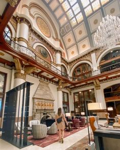 a woman is walking through the lobby of a large building with chandeliers hanging from the ceiling