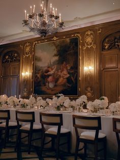 a long table with white flowers and candles in front of a painting on the wall