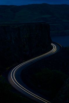 a long exposure shot of a road going through the mountains at night with lights on