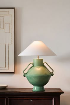 a green vase sitting on top of a wooden table next to a white lamp shade