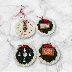 three crocheted christmas ornaments hanging on a marble surface with red and white ribbon