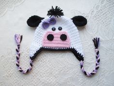 a crocheted cow hat with black ears and pink nose is laying on a white surface