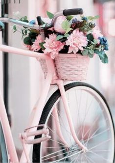 a pink bicycle with flowers in the basket parked on the side of the road next to a building