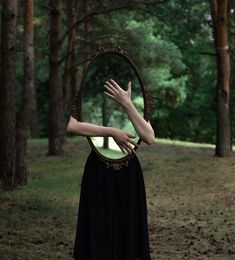 a woman with her hands on the mirror in front of her face, standing in a wooded area