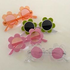 four pairs of sunglasses with flower shaped frames on white surface, one is pink and the other two are green