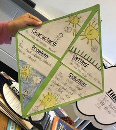 a person holding up a paper kite in front of a table with books and papers on it