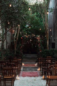 an outdoor ceremony setup with wooden chairs and candles on the aisle, surrounded by greenery