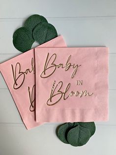 two pink napkins that say baby in bloom and one with gold lettering on them