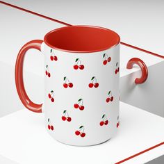 a red and white coffee mug with cherries on it sitting next to a pair of scissors