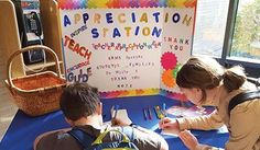 two children sitting at a table with an appreciation station sign in the background and a person writing on a clipboard