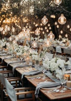 a long table set up with white flowers and hanging lights