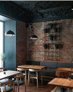 an empty restaurant with brick walls and wooden tables in the foreground, hanging planters on the wall