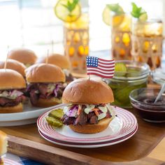 two plates with sandwiches and pickles on them, one has an american flag sticking out of it