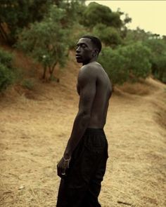 a man standing in the middle of a dirt road next to some bushes and trees