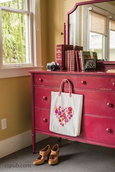 a pink dresser with a white bag and some books on it next to a pair of brown shoes