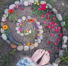 the person is standing in front of a circle made out of rocks and flowers on the ground